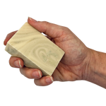 A hand holding a rectangular bar of soap with a swirled cream and light green pattern, isolated on a white background.